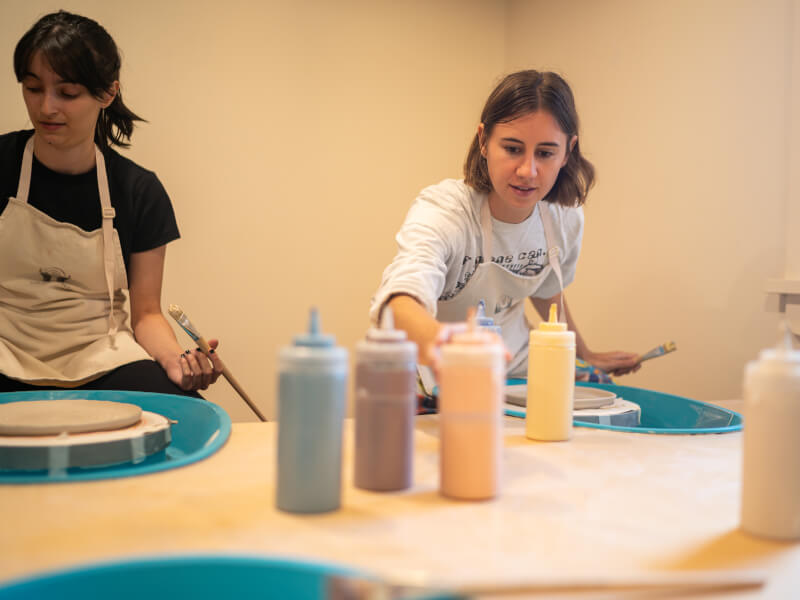 Students reaching for various colours of pottery paint in plastic squeeze bottles
